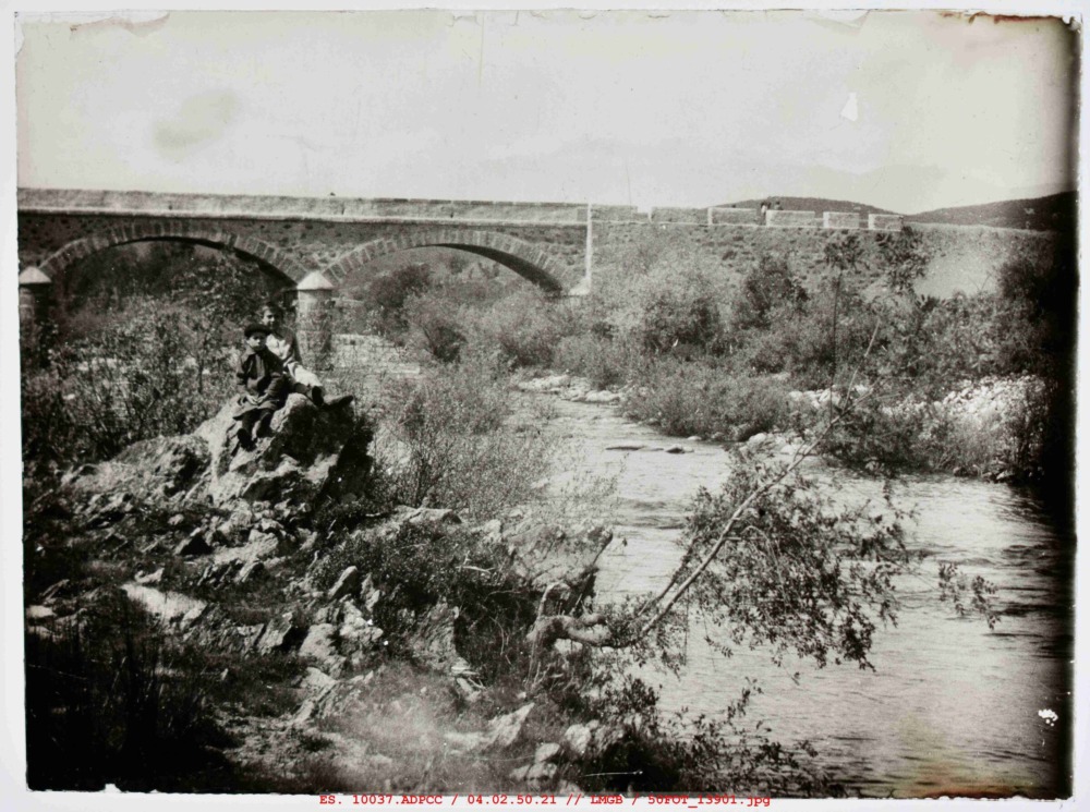 2 niños sobre una piedra delante del puente de Cuacos