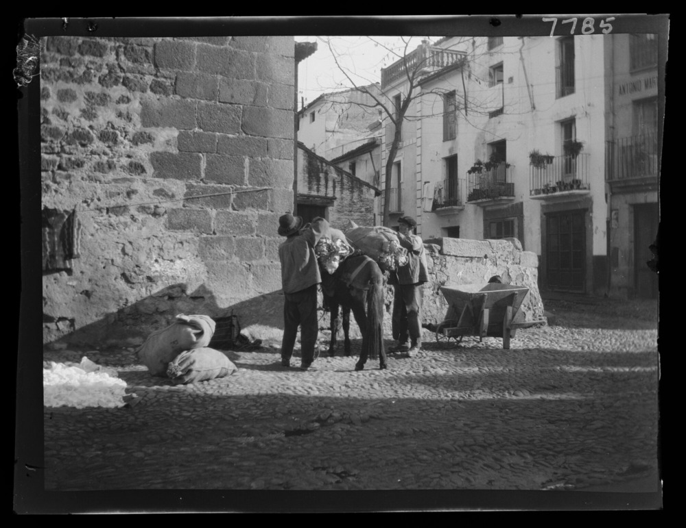 Hombres cargando un saco en una mula junto a una carretilla