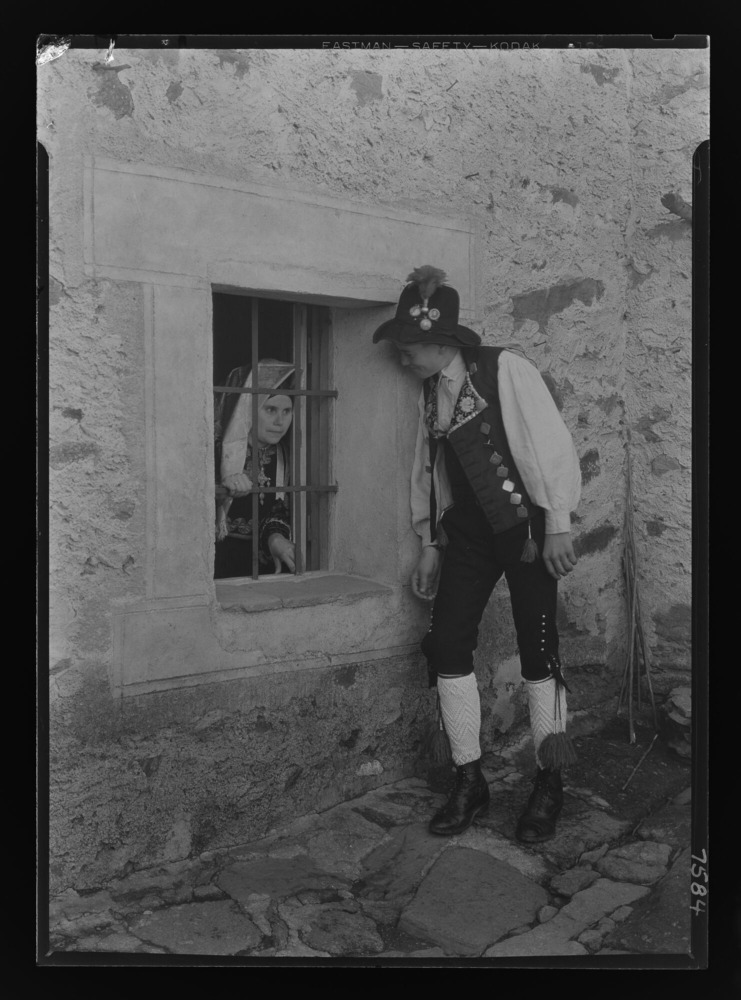 Miguel, con sombrero de fieltro negro, ante la ventana de una mujer