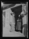 Mujer a la puerta de una tienda de comestibles con dos panes y bacalao seco expuestos · Ruth Matilda Anderson, 1928