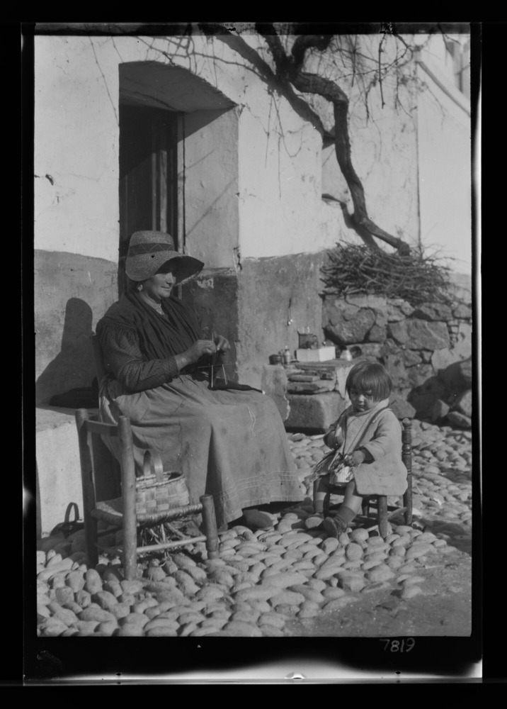 Mujer con gorra haciendo punto, con una niña sentada a su lado